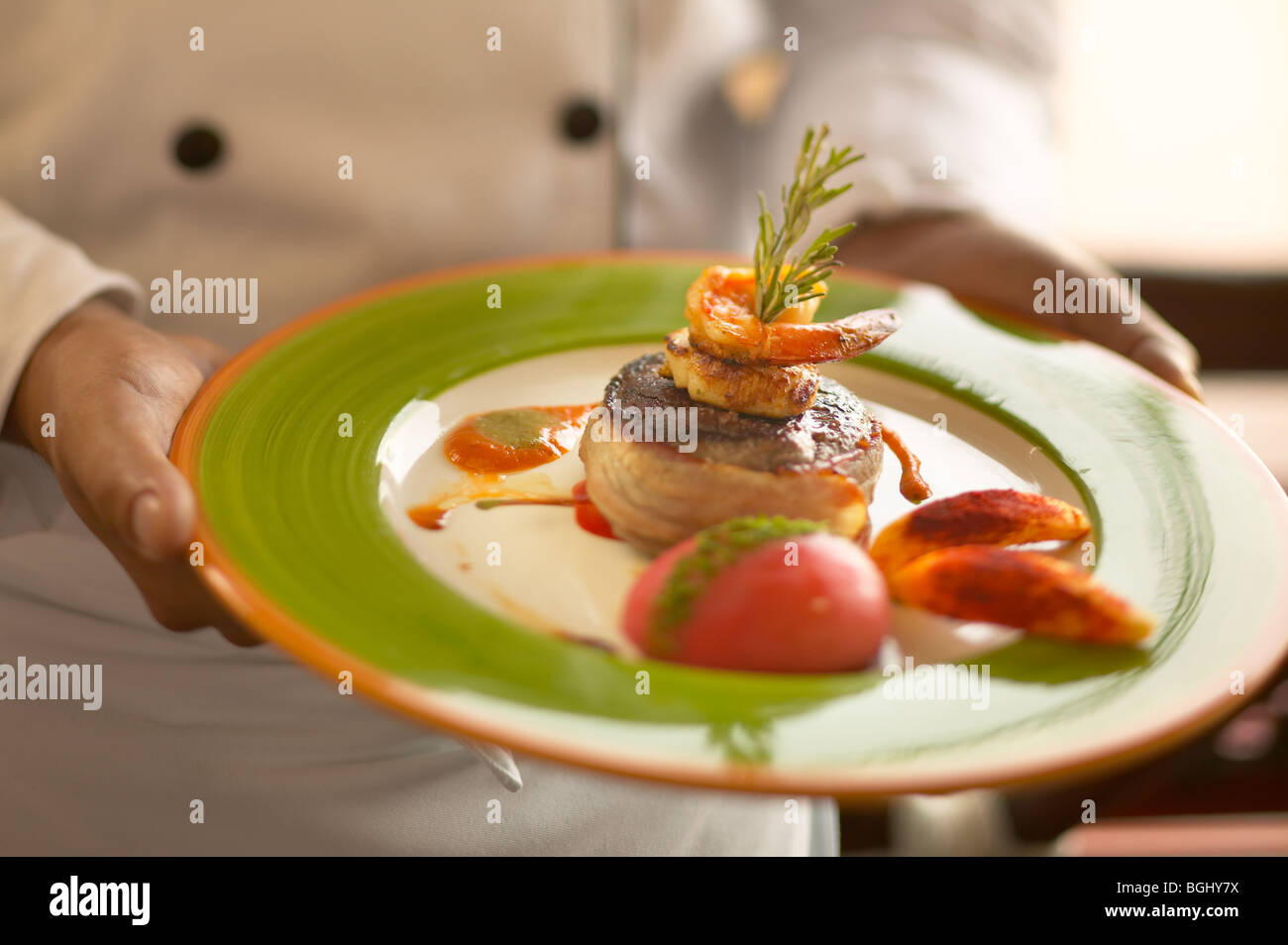 Chef holding a filet mignon wrapped with bacon topped with grilled shrimp. Side of tomato and potatoes. Stock Photo