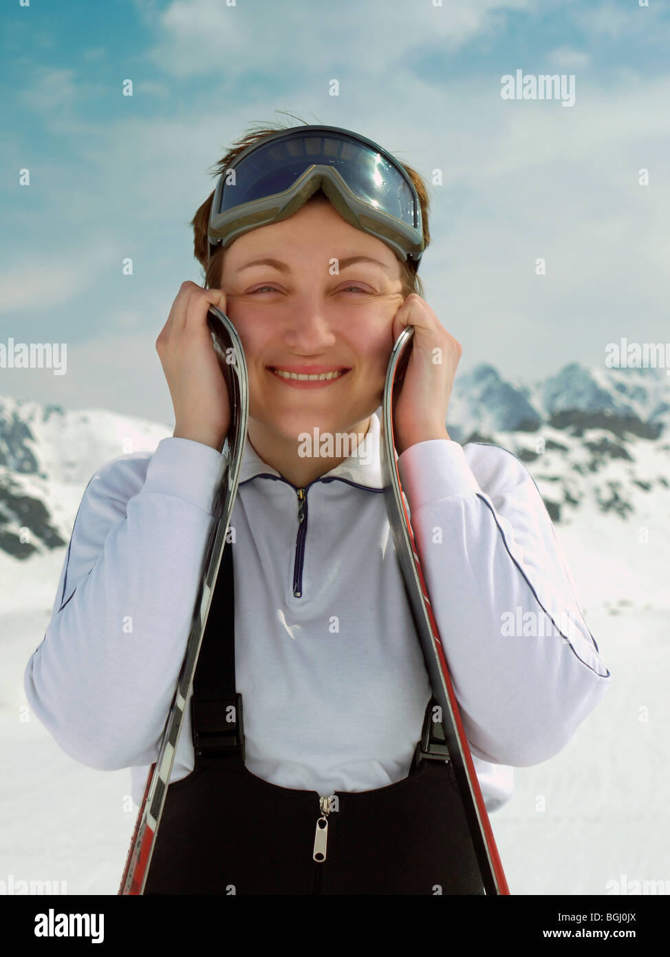 Young attractive female skier posing with her skis with mountain range in the background Stock Photo
