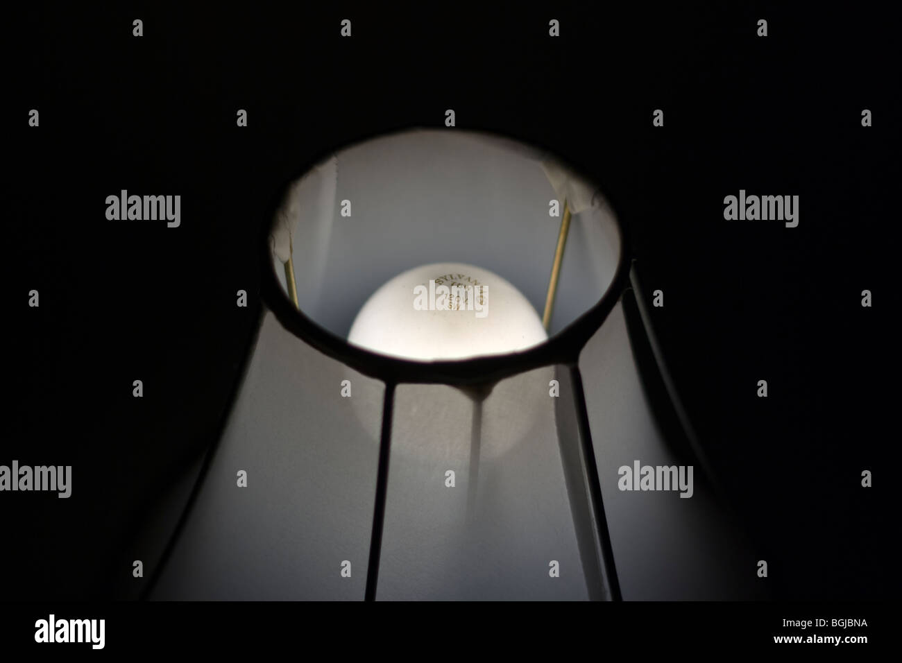 Sylvania, 75 Watt, 120 Volt Lightbulb illuminated inside of a sheer lampshade. Stock Photo