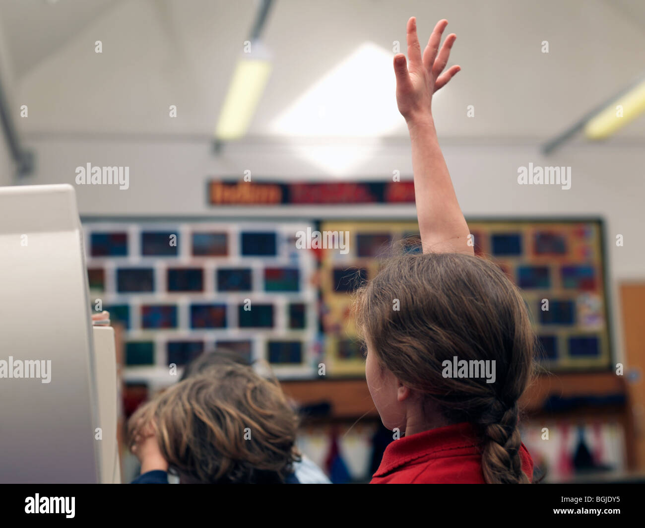 child raising hand in classroom to answer question Stock Photo