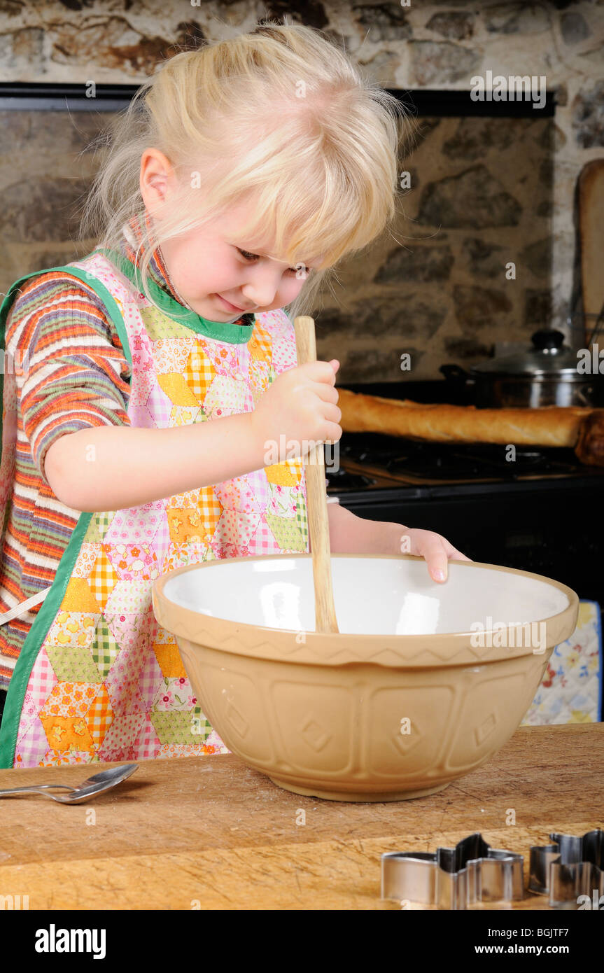 Stock photo of a four year old girl using a wooden spoon to mix up some