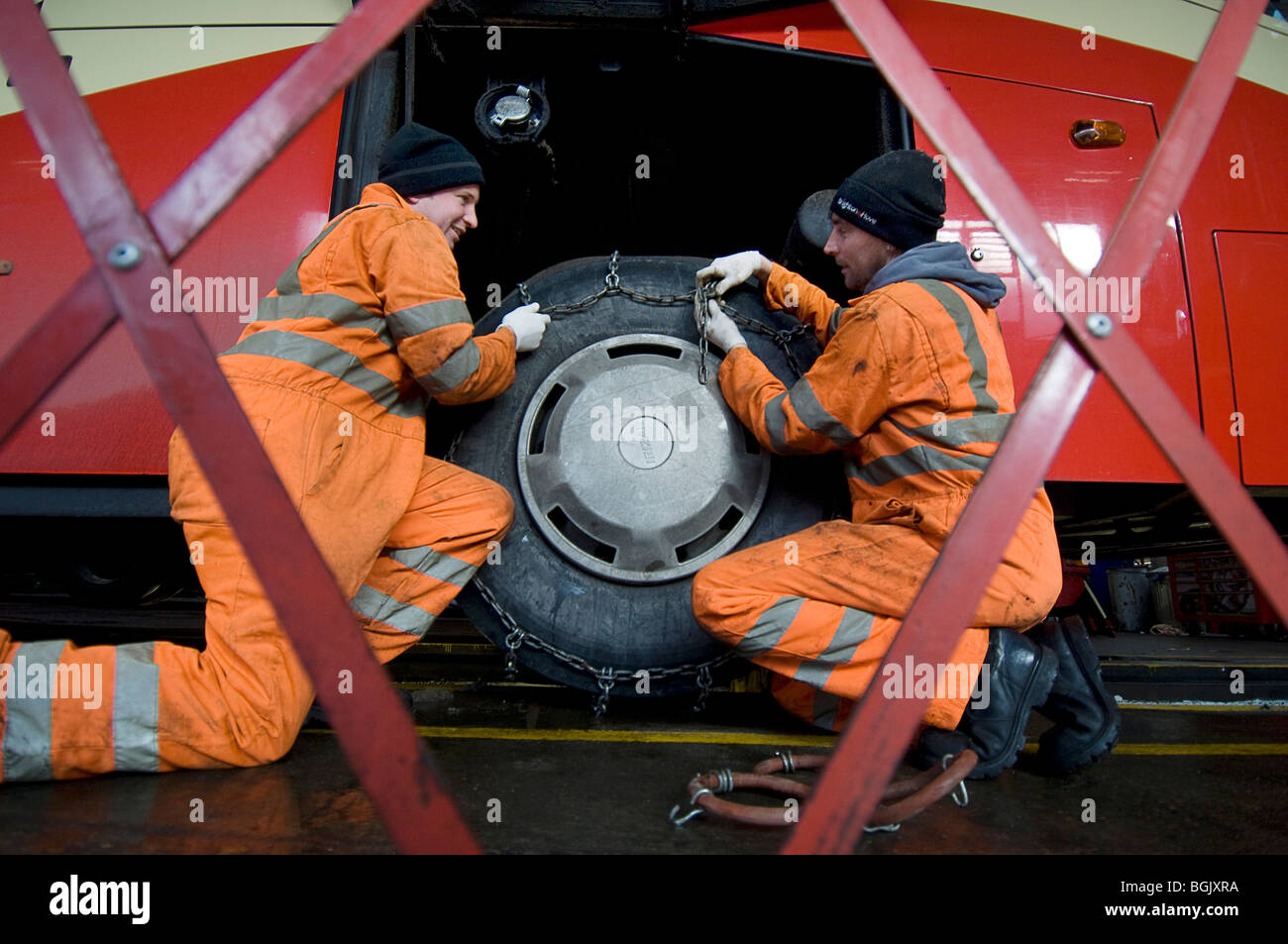 Two mechanics fitting snow chains to a bus wheel using a bus garage inspection pit Stock Photo