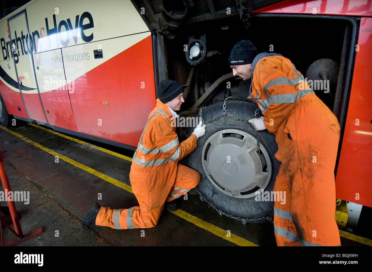 Two mechanics fitting snow chains to a bus wheel using a bus garage inspection pit Stock Photo
