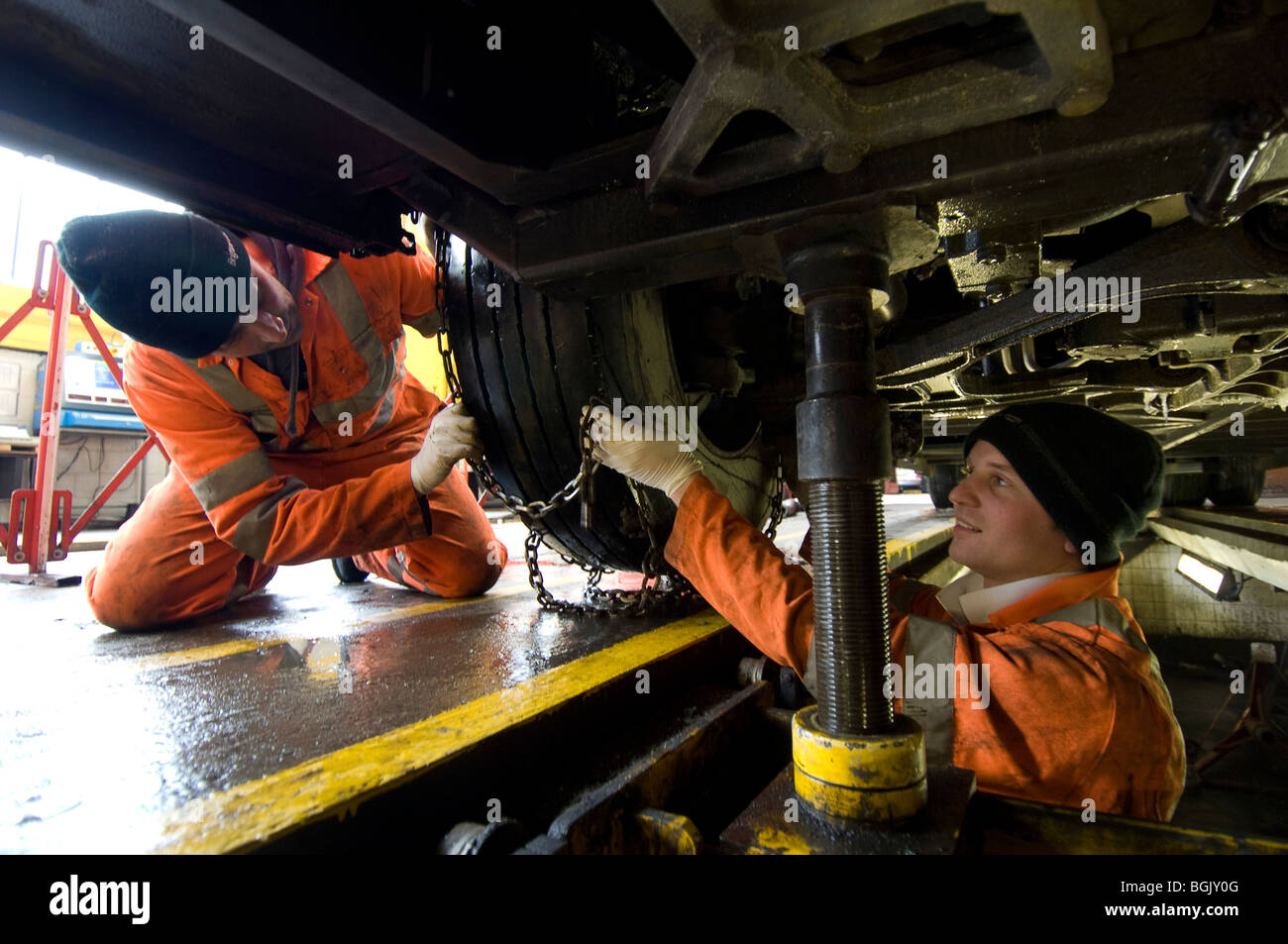 Two mechanics fitting snow chains to a bus wheel using a bus garage inspection pit. Stock Photo