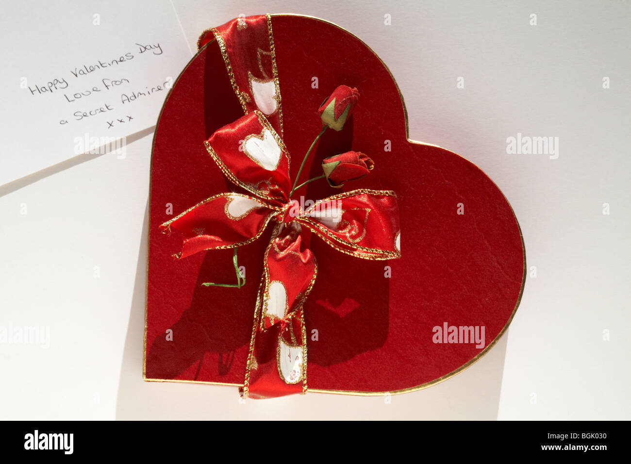 Gold rimmed red heart shaped box with ribbon and red roses and message from secret admirer for a Happy Valentines Day, Valentine day Stock Photo
