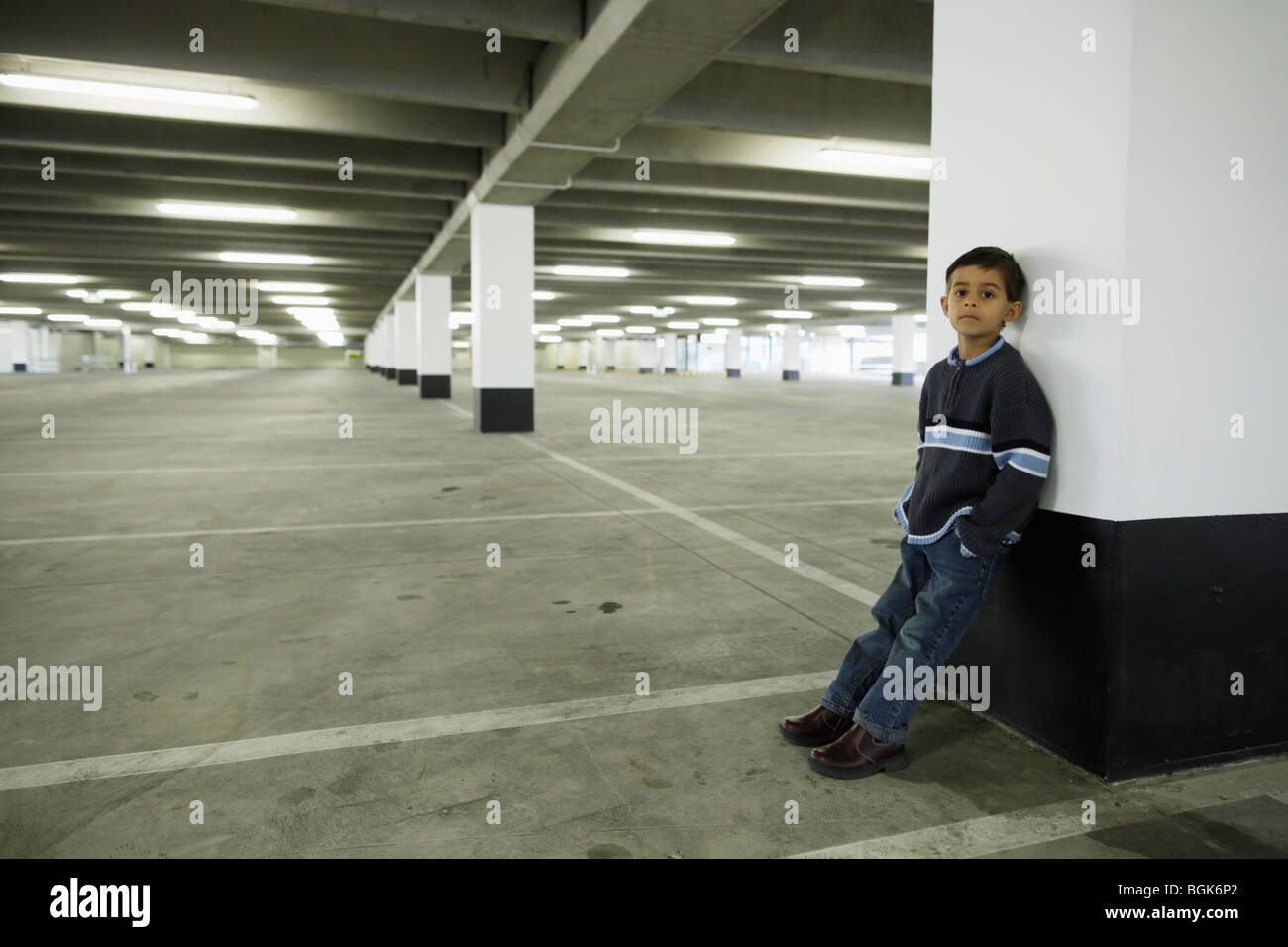 Boy leans against concrete pillar in empty car park Stock Photo