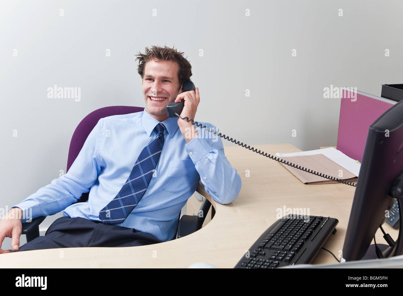 A businessman wearing shirt and tie sat at his desk chatting on the telephone. Stock Photo