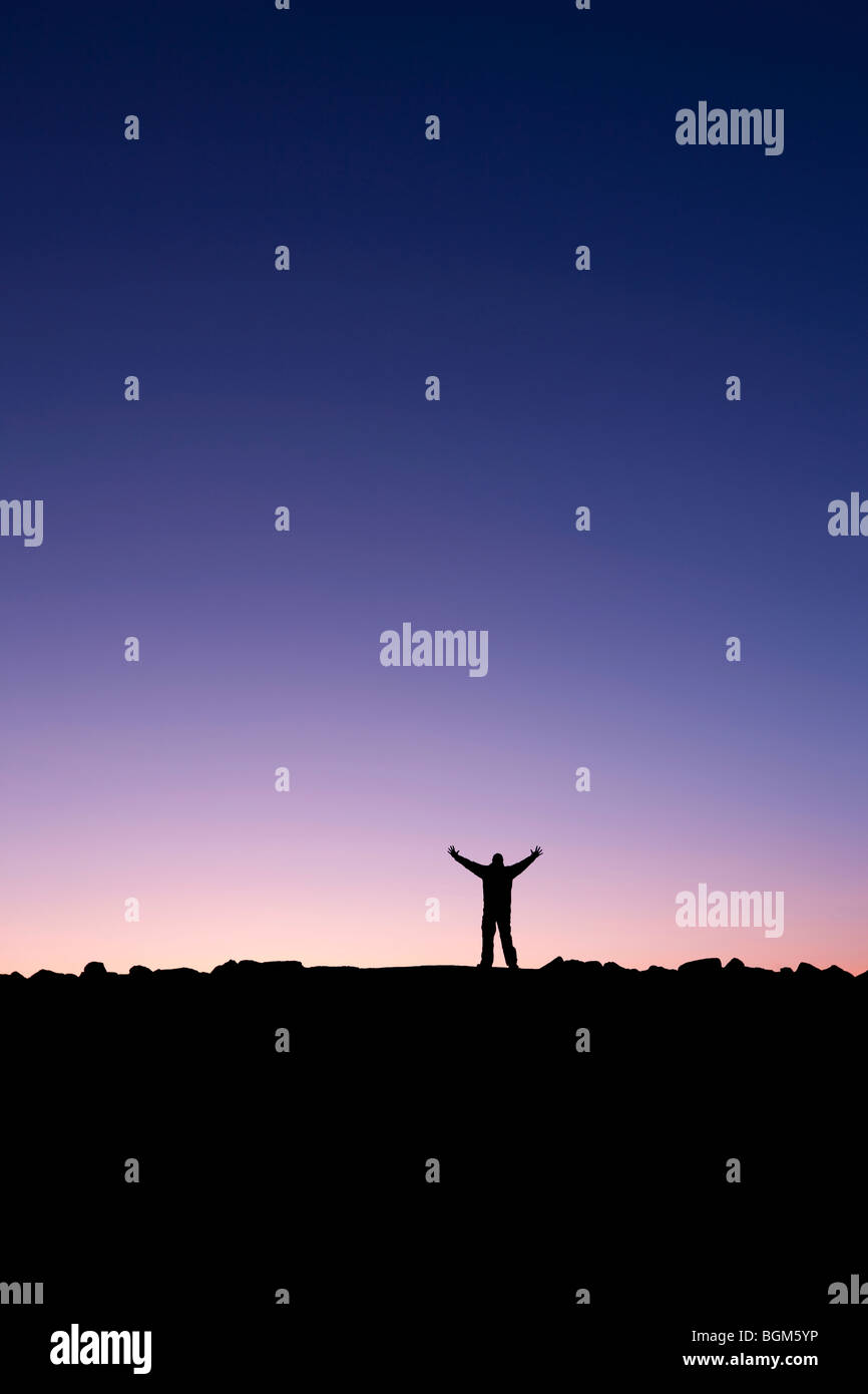 Silhouette of a man raising his hands into the sunrise after conquering a summit Stock Photo