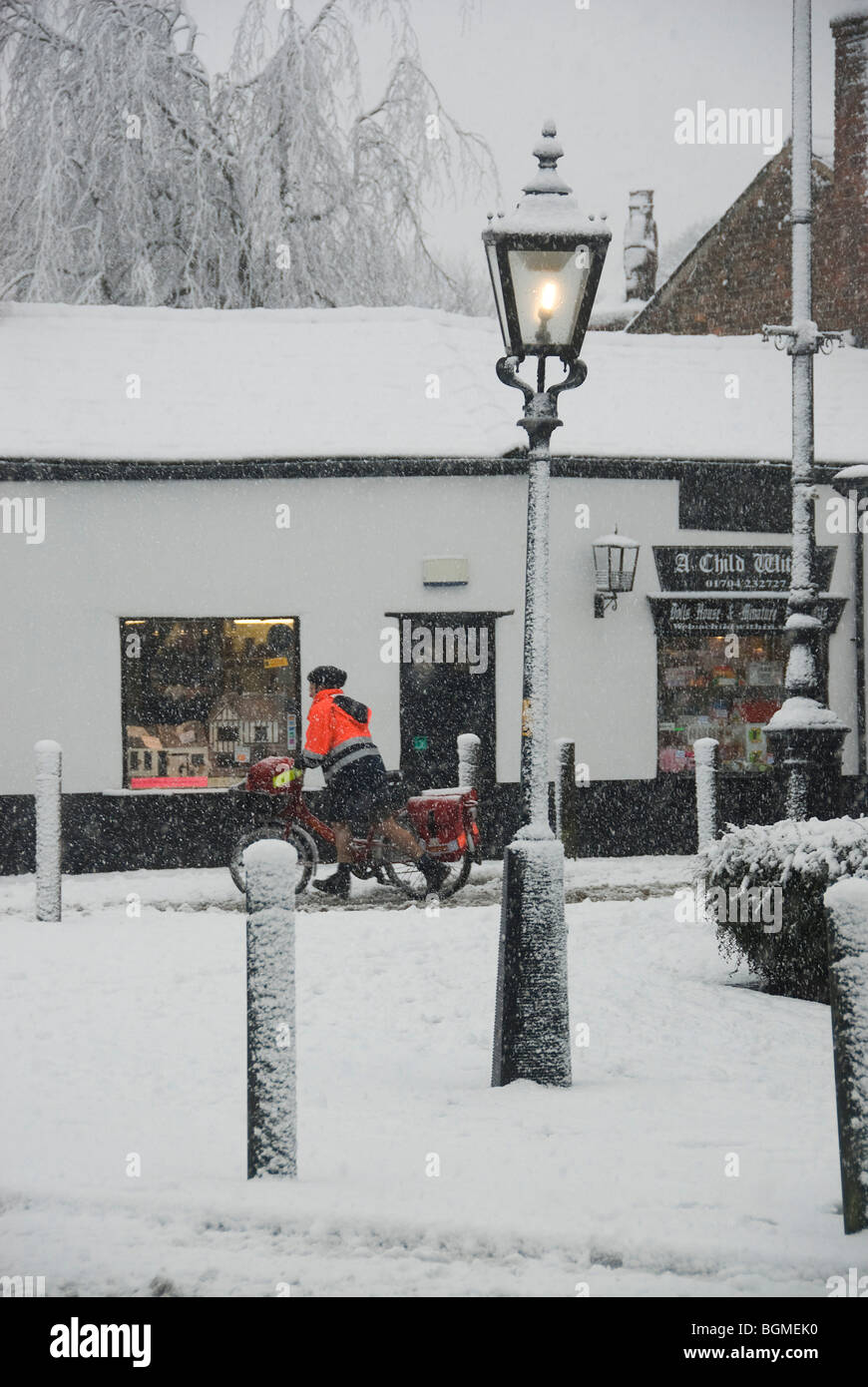 Postman on his round in wintry village scene. Stock Photo