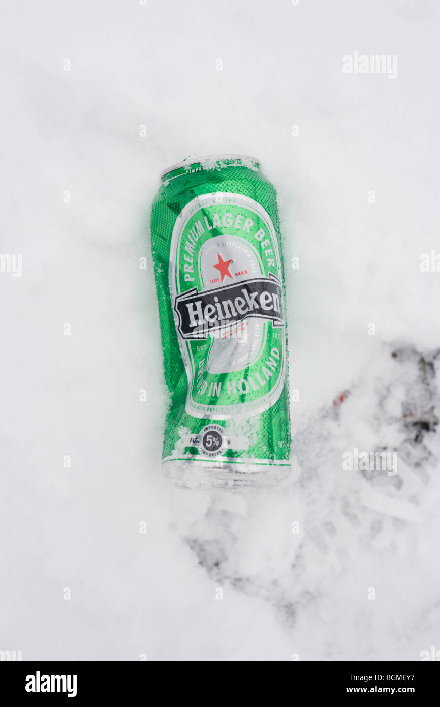 A partially-crumpled Heineken premium beer can left in fresh snow. Stock Photo