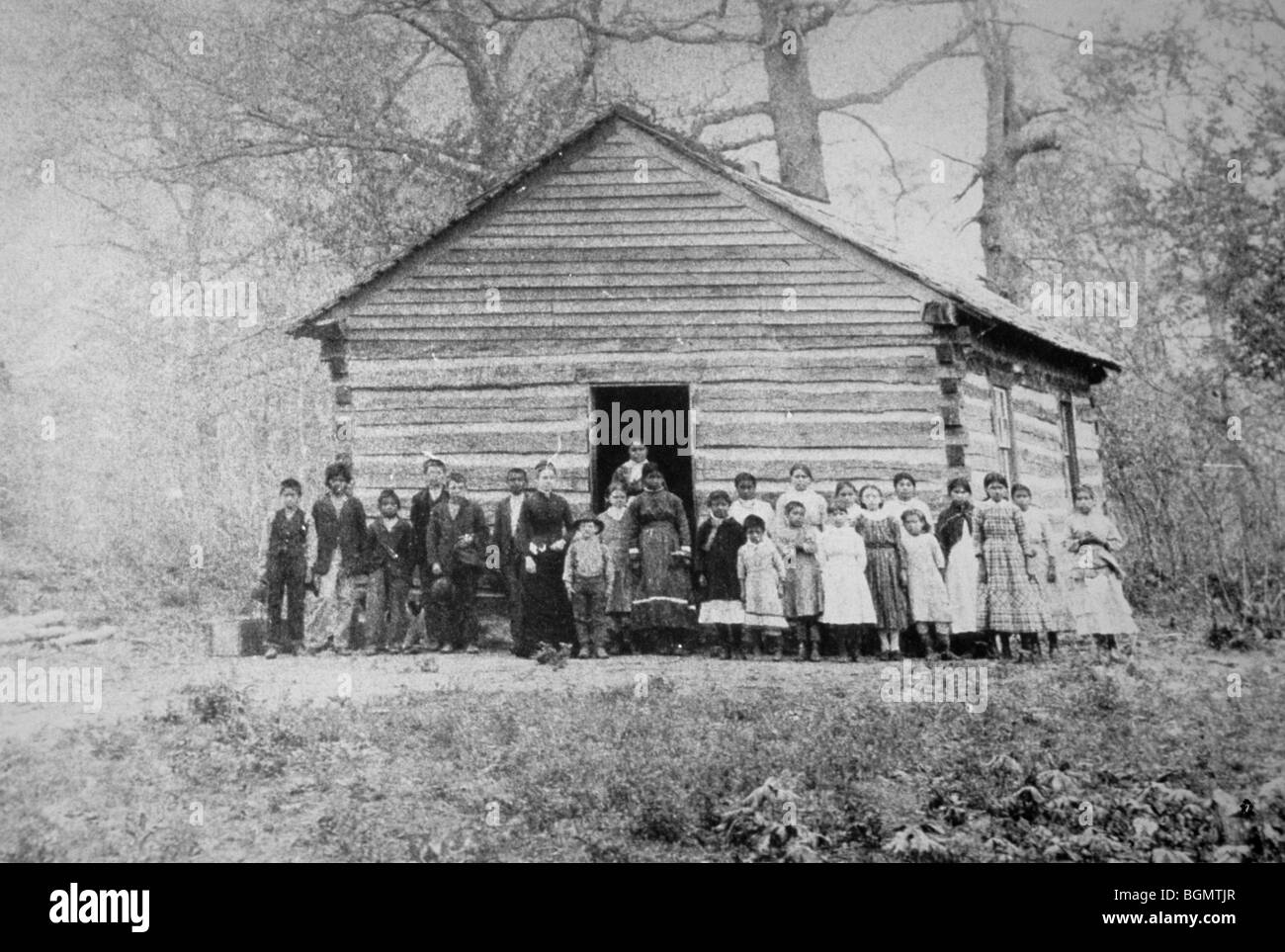Historic photograph of Cherokee children standing in front of a school house built from logs located in Indian Territory, now known as Oklahoma Stock Photo
