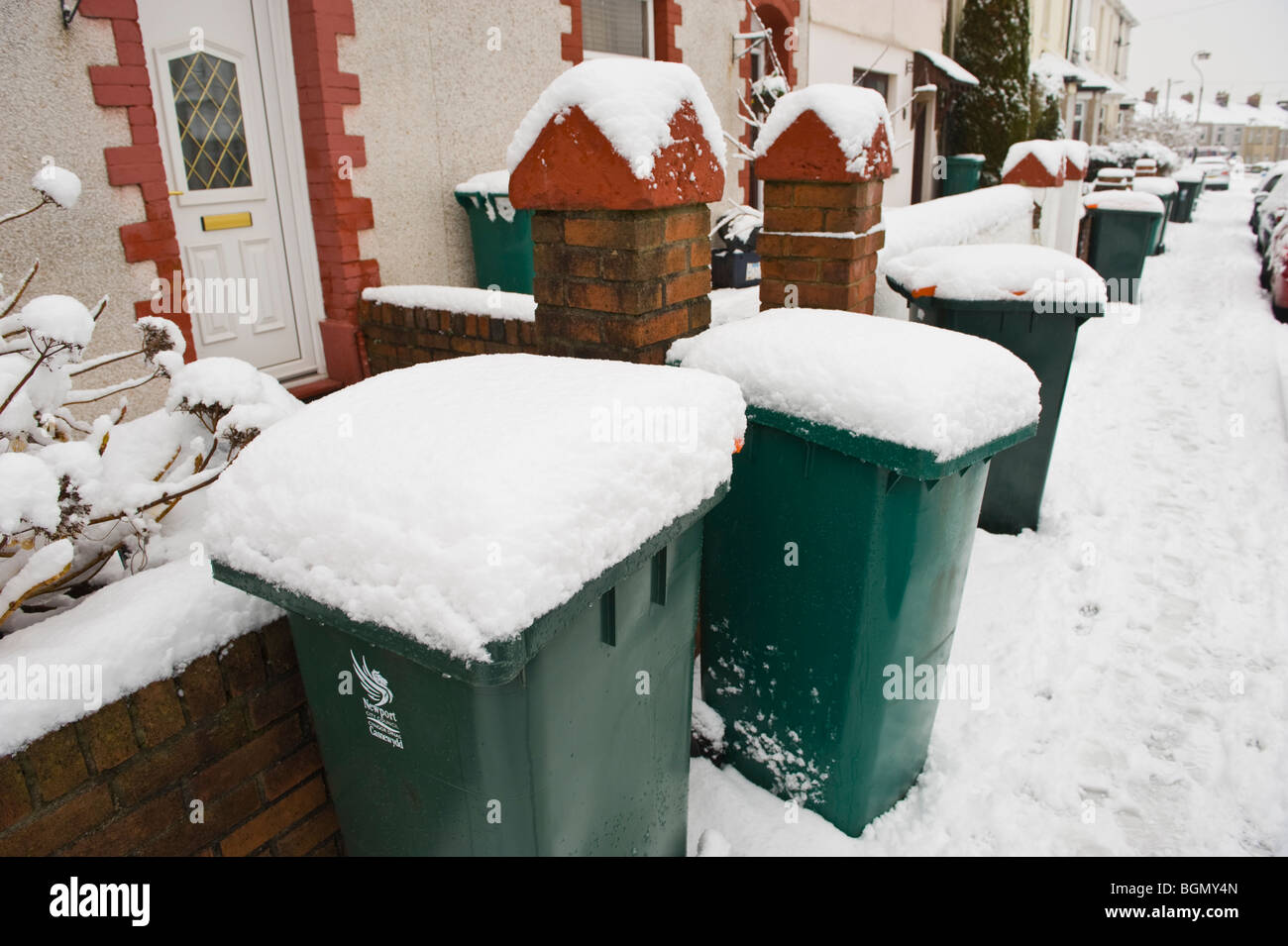 Wheelie bins covered in winter snow outside terraced houses in Newport