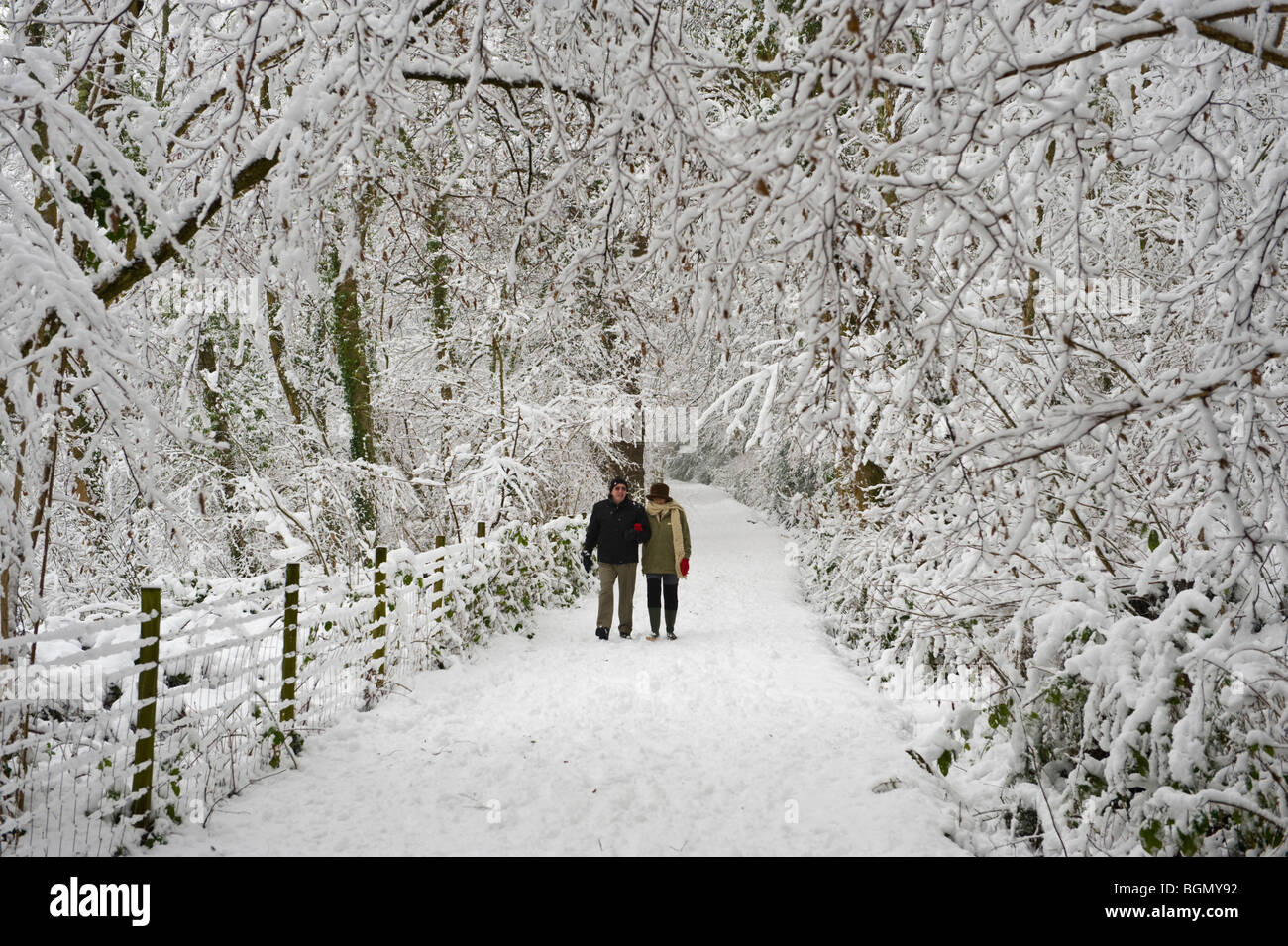 Two people walking down footpath after winter snow at Allt Yr Yn Nature Reserve Newport South Wales UK Stock Photo