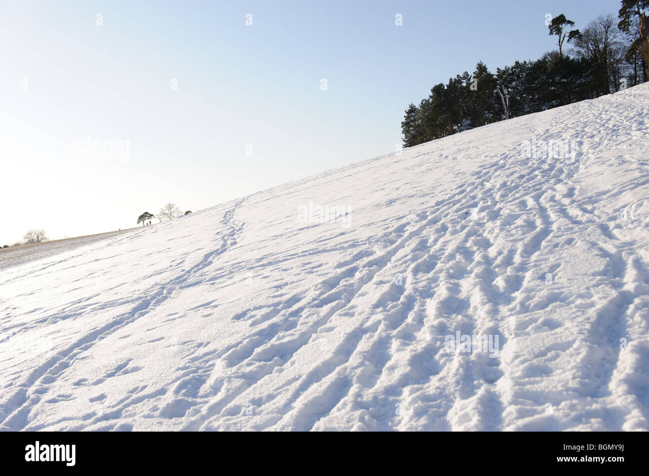 Snow landscape scenic field winter Christmas hill white ice cold blue sky trees hedgerow footprints sledge sledging Stock Photo
