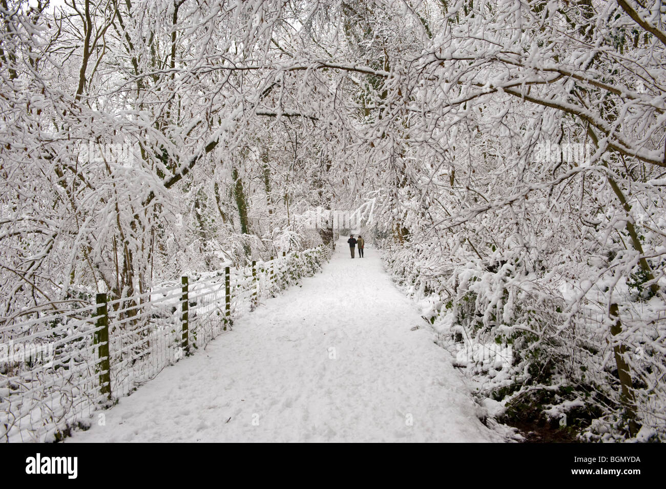 Two people walking down footpath after winter snow at Allt Yr Yn Nature Reserve Newport South Wales UK Stock Photo