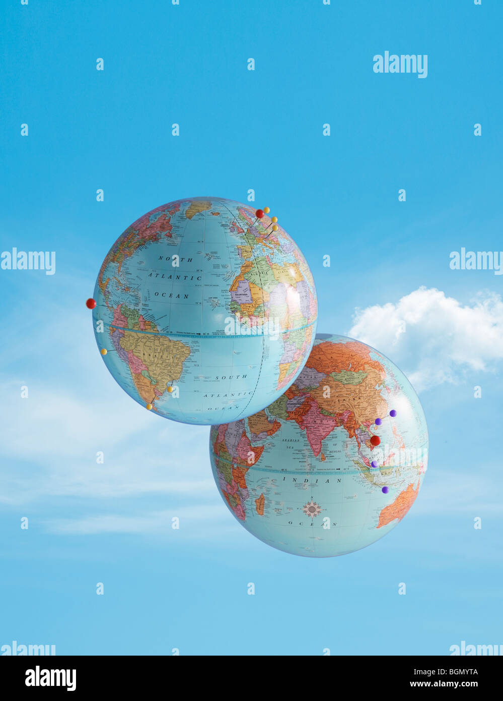 two globes floating in the sky with pins marking destinations of travel Stock Photo