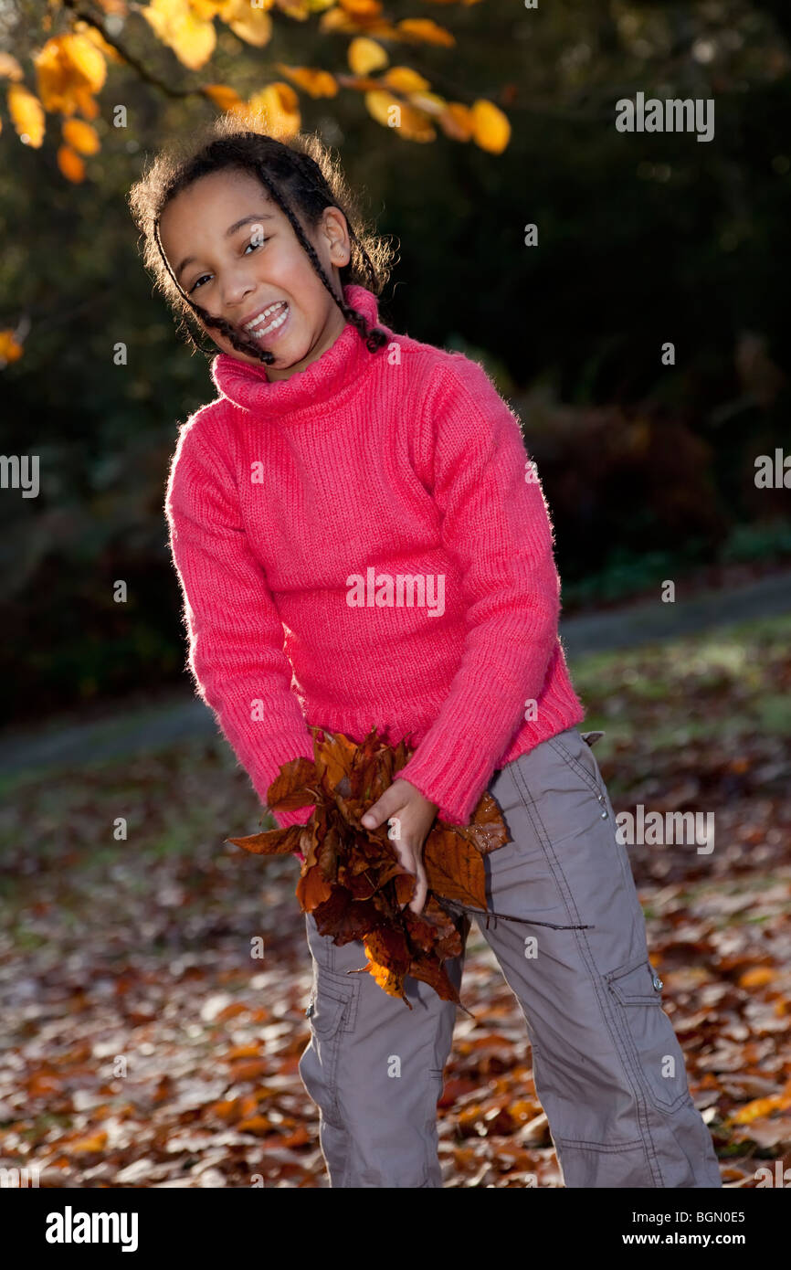 Photograph of a beautiful young smiling happy mixed race interracial African American girl playing with leaves during the fall Stock Photo