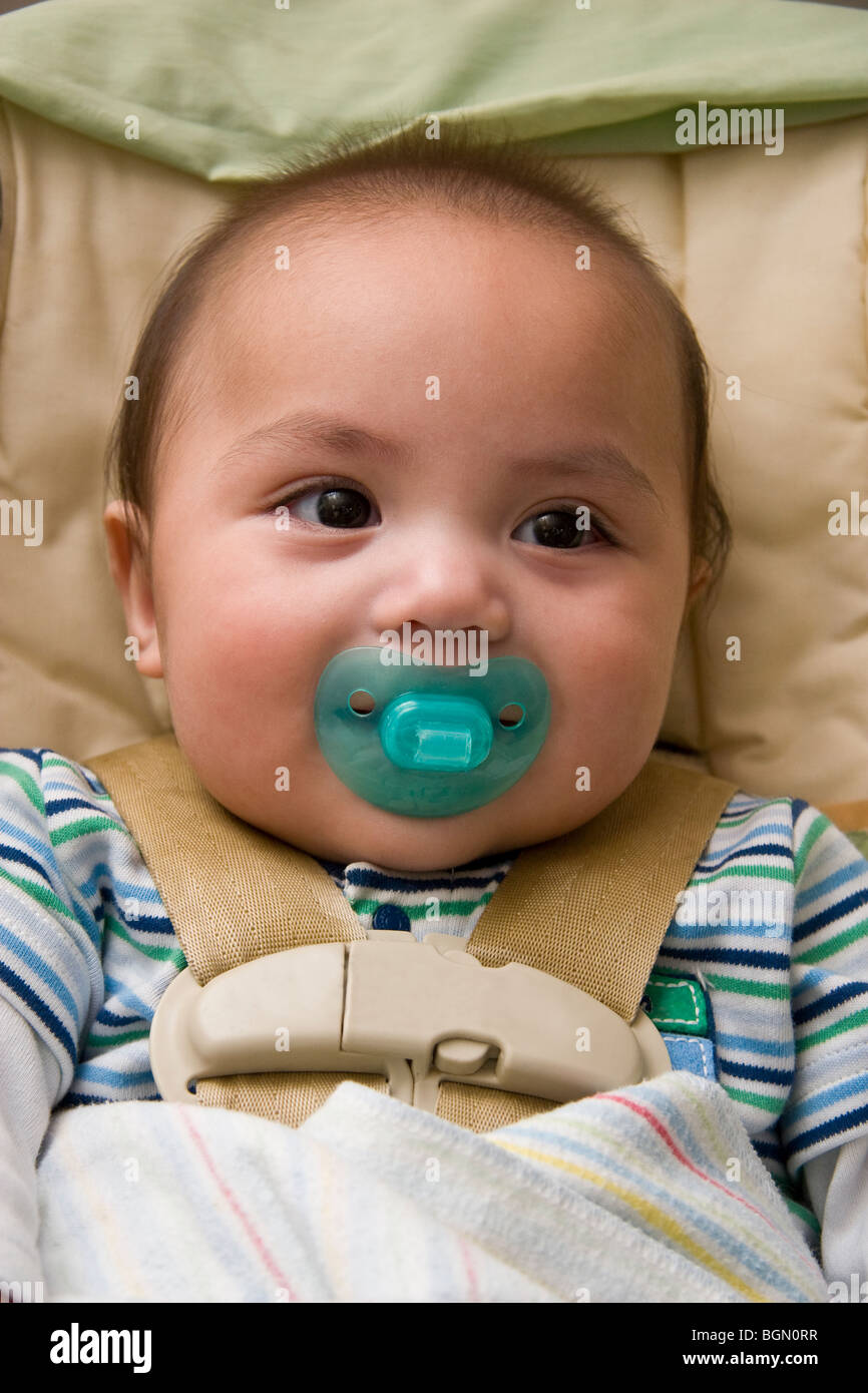 Healthy Native American infant sucking on a pacifier happily sits inside his car seat Stock Photo