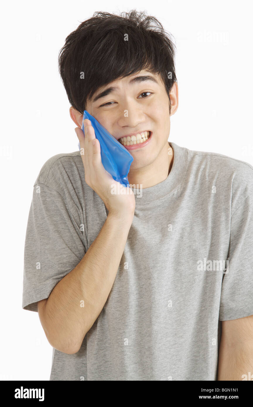 Young man having toothache and pressing a ice pack on his cheek Stock
