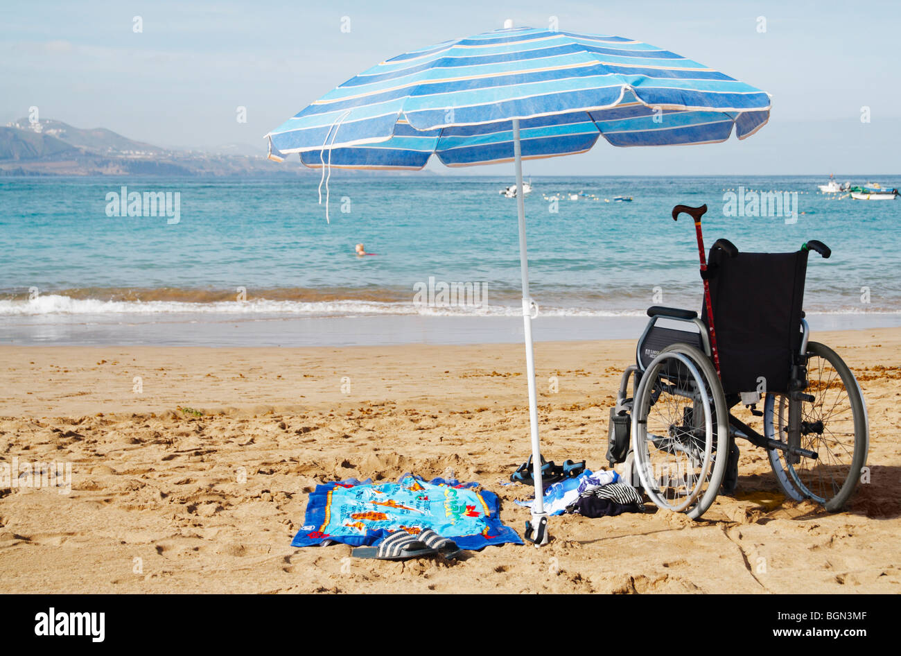 Disabled person swimming in sea in Spain with wheelchair on beach. Stock Photo