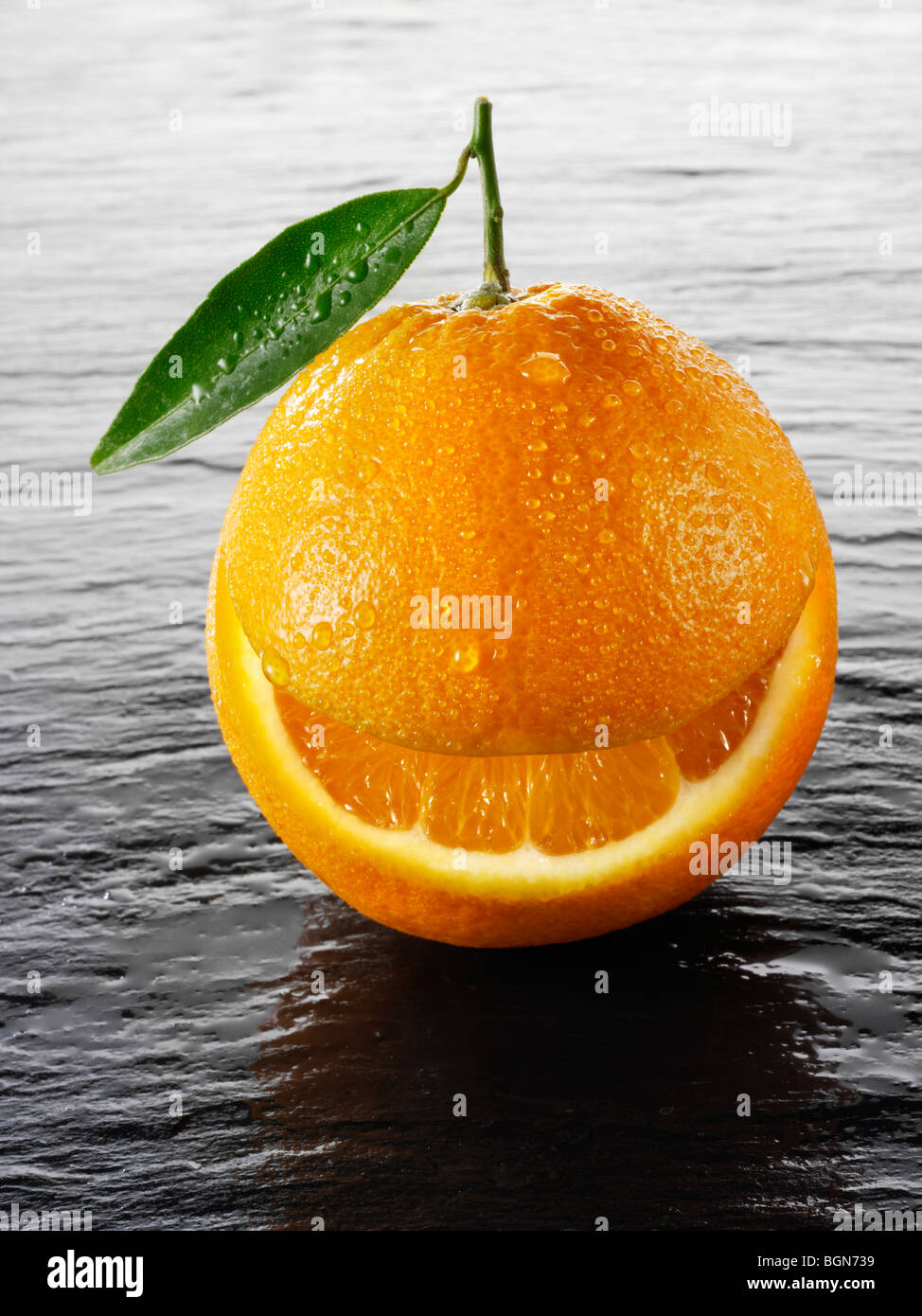 Wole oranges with a smiley face on a black background  with leaves Stock Photo