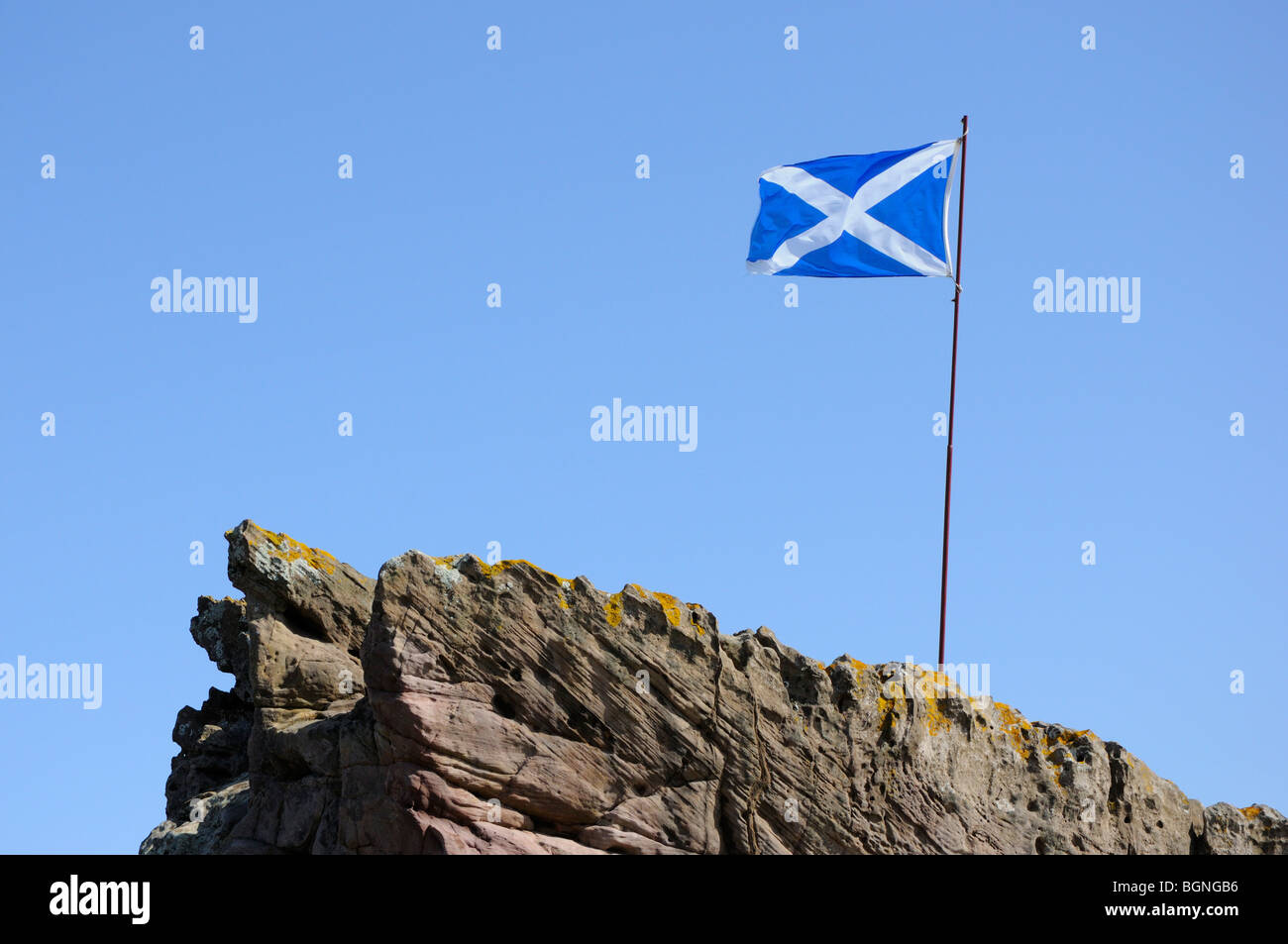 Scottish national flag flying above a rocky outcrop, Scotland, UK. Stock Photo