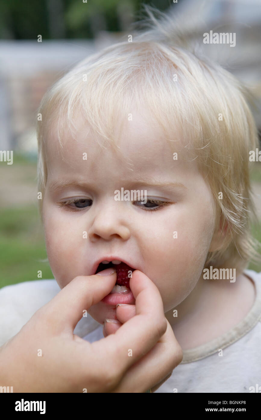portrait of little cute blond serious baby girl. Mother feed her ...
