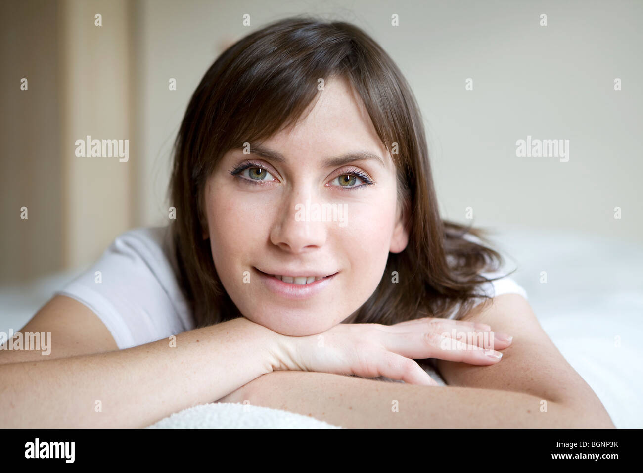 portrait of brunette smiling woman lying on bed on her stomach Stock ...