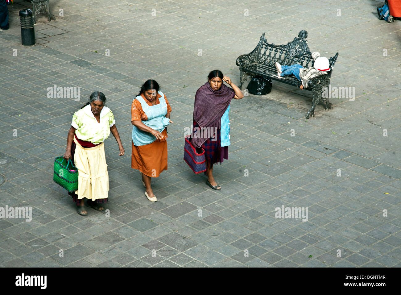 three indigenous Indian women conversing earnestly cross the plaza of the Zocalo in the central district of Oaxaca City Mexico Stock Photo