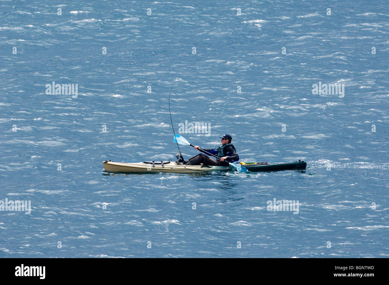 Man in sea kayak paddling on the Atlantic Ocean while dragging fishing line along Stock Photo