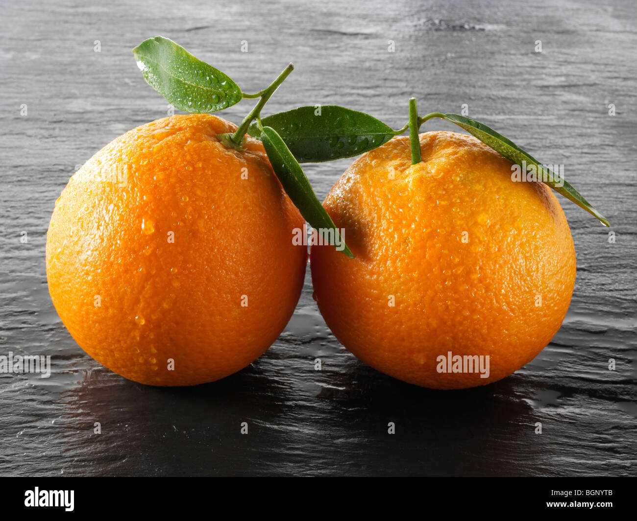 Whole and cut fresh oranges with leaves against a black background Stock Photo