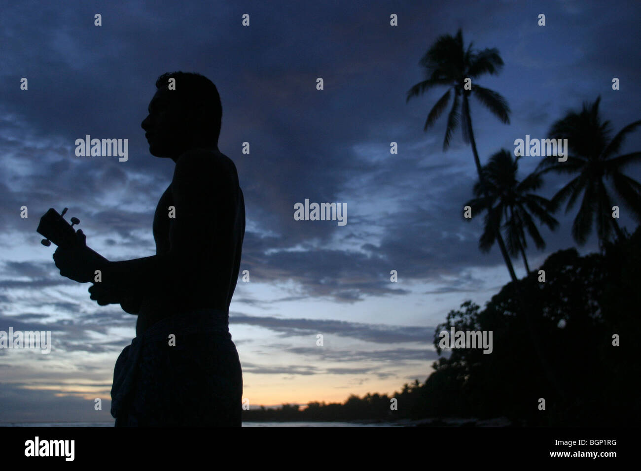 playing guitar and singing next to the sea, at dusk, on Kiribati atoll. Stock Photo