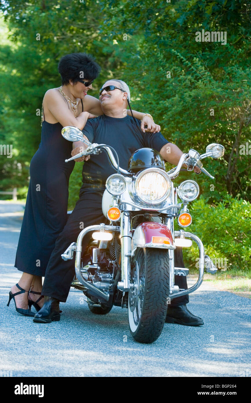 Senior man sitting on a motorcycle with a mature woman standing beside him Stock Photo