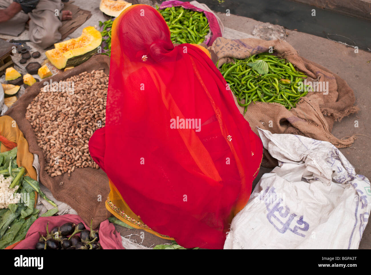 Rajasthani woman in red and yellow saree, sari selling nuts and green chillies in Jaipur market, Rajasthan, India Stock Photo
