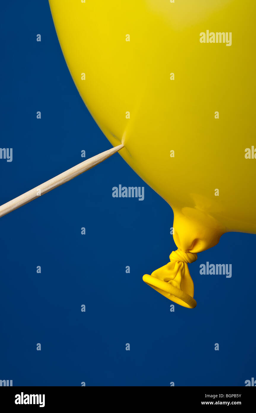 a pointed stick ready to pop a yellow balloon on blue Stock Photo