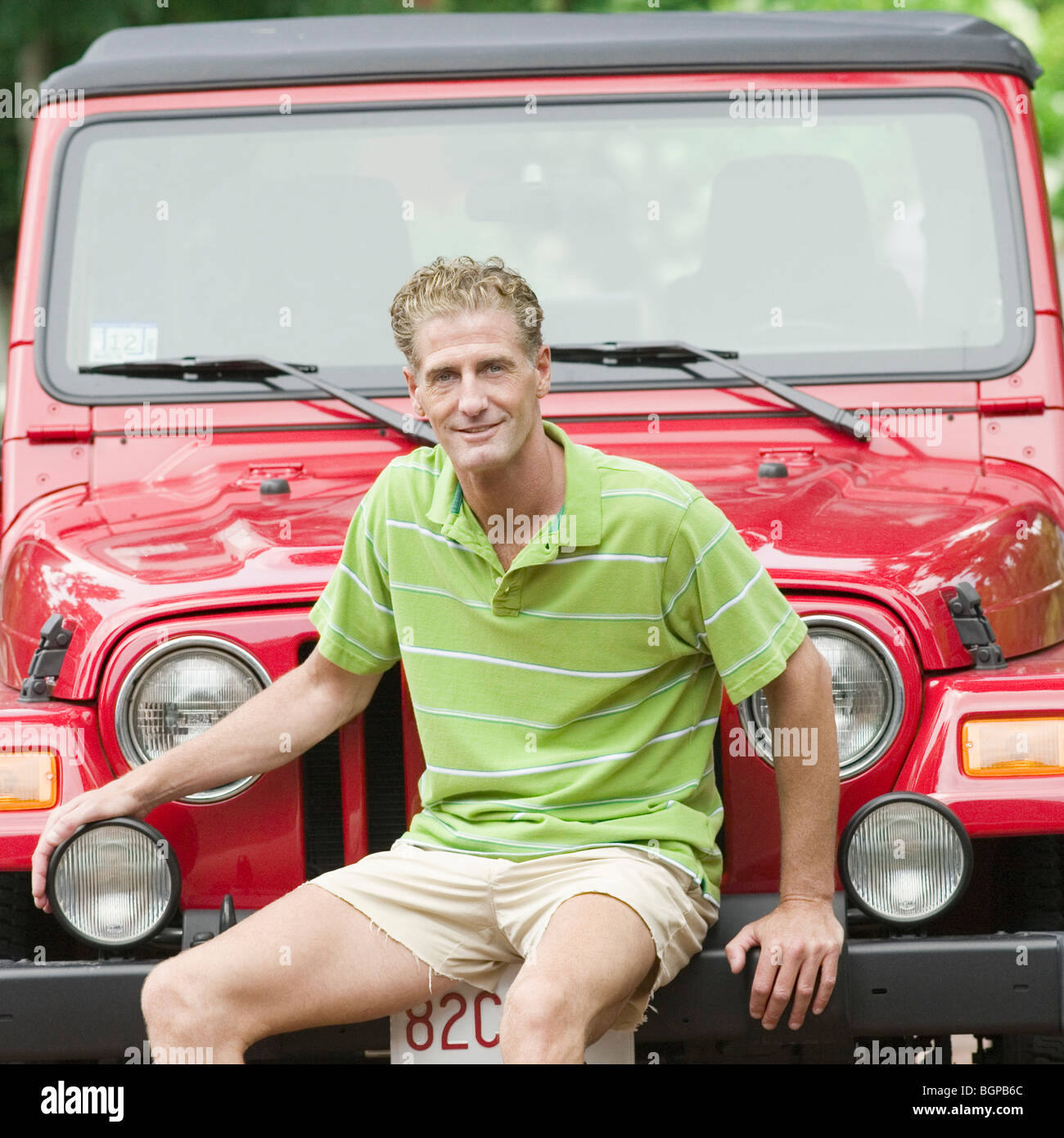 Portrait of a mature man sitting on the bumper of a jeep and smiling Stock Photo