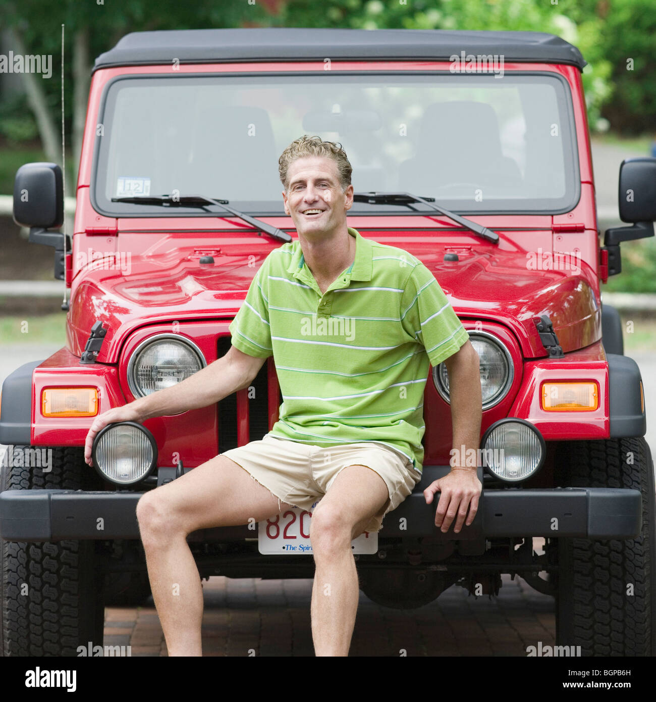 Portrait of a mature man sitting on the bumper of a jeep and smiling Stock Photo