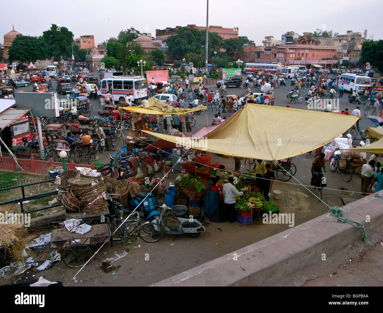 Jaipur traffic at cross roads, with vegetable vendors under canopy in foreground. Stock Photo