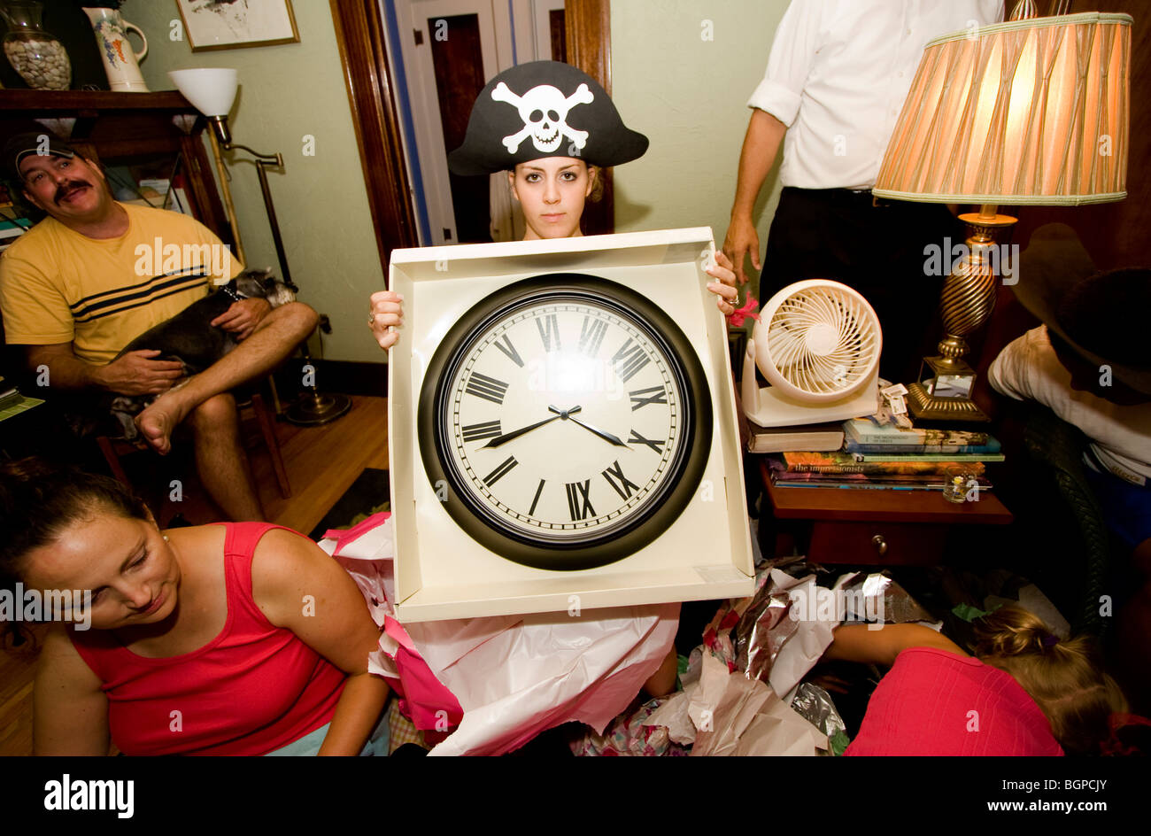 A woman wearing a pirate hat holds up a clock given as an anniversary gift. Stock Photo