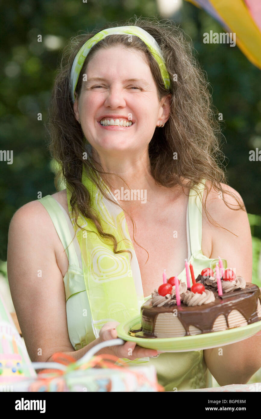 Mature woman holding a birthday cake and smiling Stock Photo - Alamy