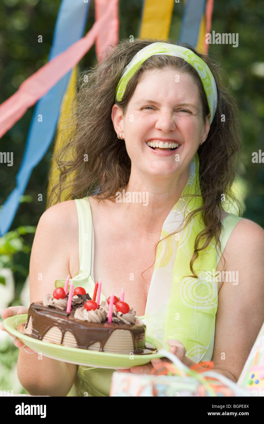 Mature woman holding a birthday cake and smiling Stock Photo - Alamy