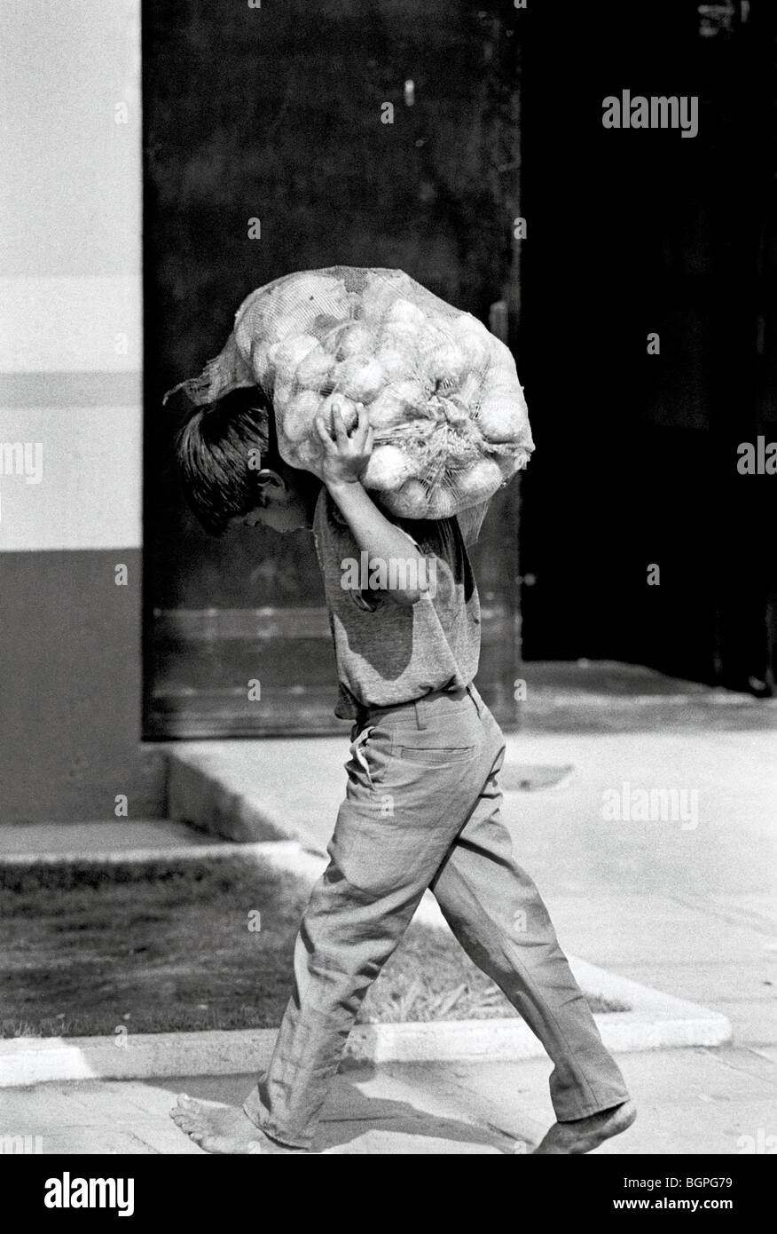 Young boy carrying heavy bag of potatoes on his shoulder Mexico city