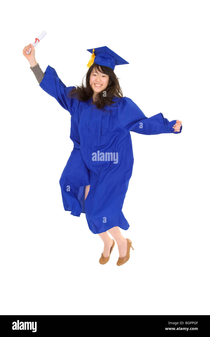 An Asian teenage in blue graduation gown and smiling and jumping in joy. She is on a white background. Stock Photo