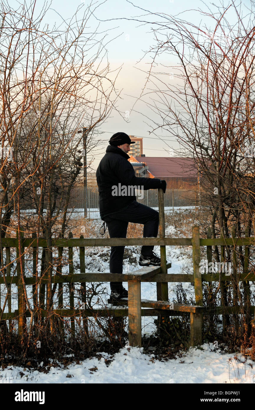 Man crossing snow covered stile Gillespie Park Highbury North London England UK Stock Photo