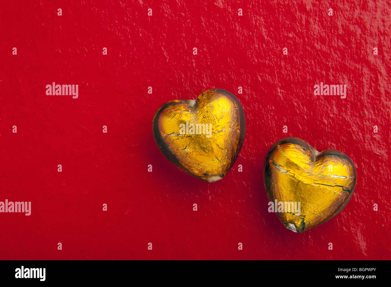 Two Gold Glass Heart Beads on red background Stock Photo