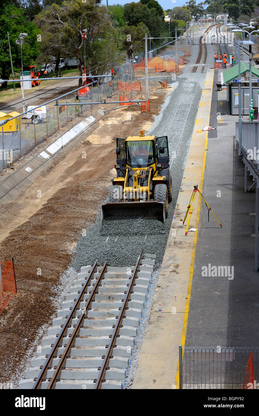 Front-end loader spreading blue-metal aggregate over new concrete sleepers on railway track. Stock Photo