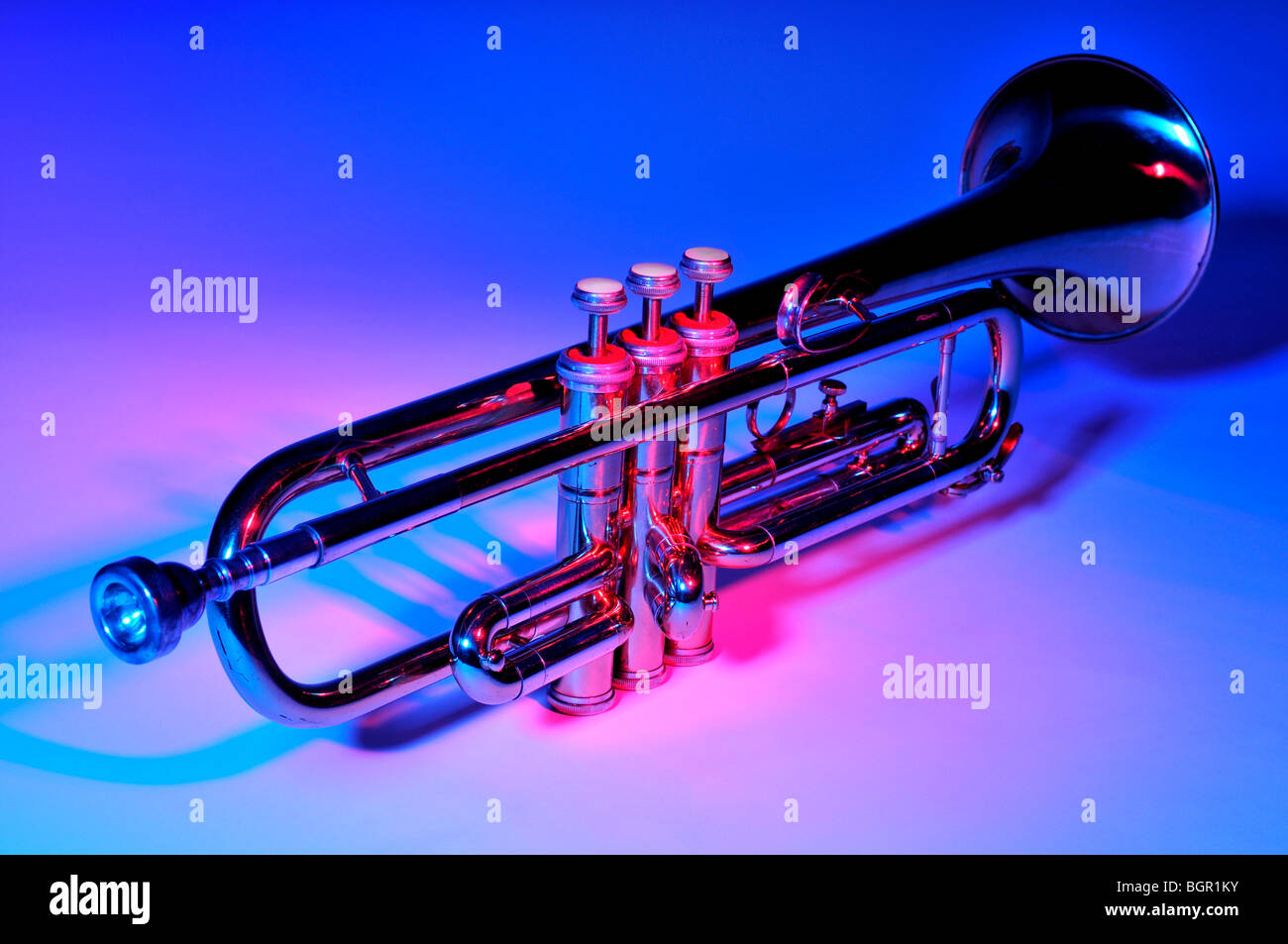 Trumpet under coloured lighting showing the mouth piece in the foreground and the bell in the background. Stock Photo