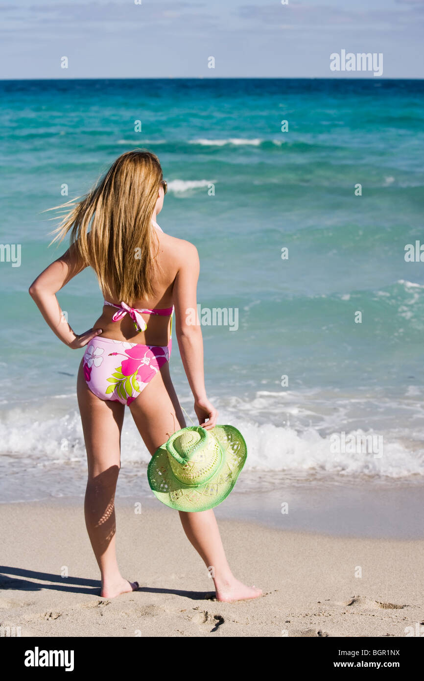 Beautiful Caucasian female teenage standing in the surf wearing a colorful one piece swimsuit. Stock Photo