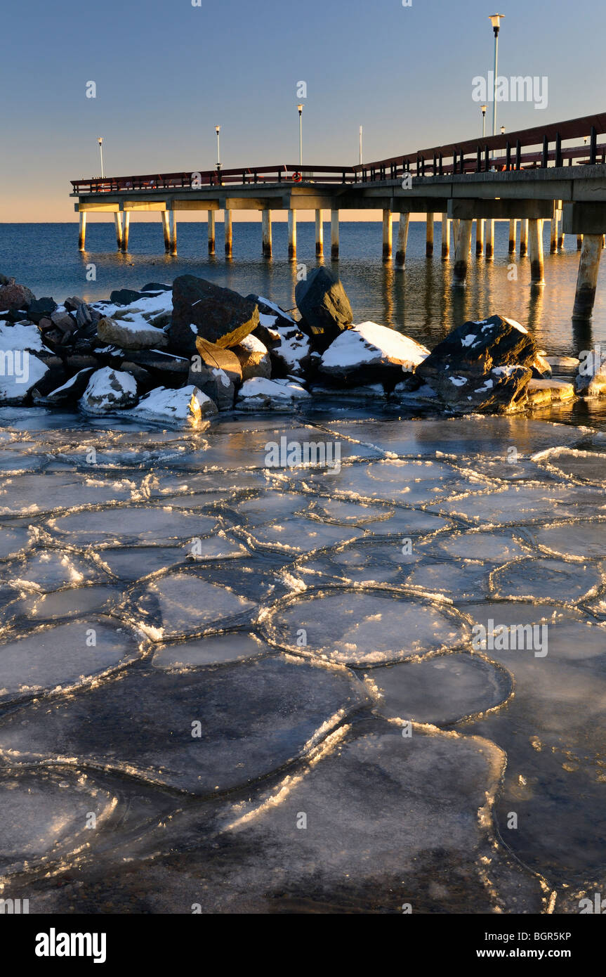 Sunset at Toronto Center Island Pier in winter with ice flows mosaic and pylon reflections on Lake Ontario Stock Photo