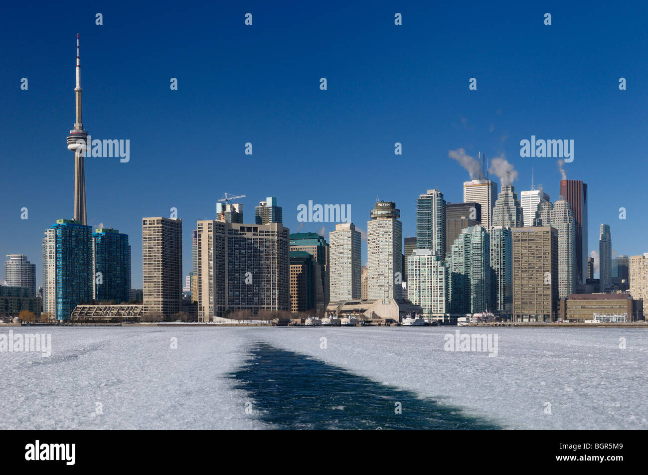 Wake of a winter ferry to the Toronto Islands keeping a channel open on an ice covered Lake Ontario with city skyline and ice slush Stock Photo